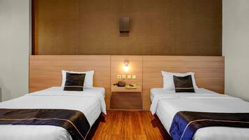 Une chambre d’hôtel avec deux lits, une tête de lit en bois, une table de chevet avec une lampe et une petite étagère avec un téléphone et un livre.