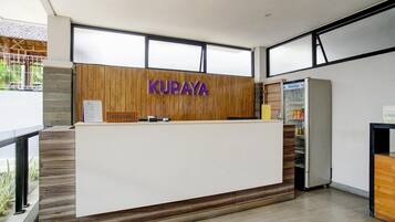 A reception desk with a wooden panel and 'KURAYA' sign, a refrigerator, and a windowed wall.