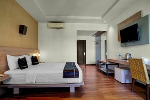 Een hotelkamer met een bed, nachtkastje, televisie, bureau, stoel en een kleine koelkast.