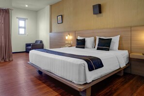 Habitación de hotel con una cama grande, un escritorio, una silla, una ventana con cortinas y una lámpara fijada a la pared.