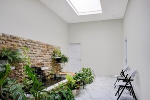Ein Zimmer mit einer Steinwand, einem kleinen Wasserspiel und verschiedenen Topfpflanzen.