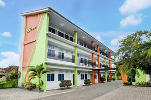 Un hotel de varios pisos con balcones, fachada verde y naranja y un patio empedrado.