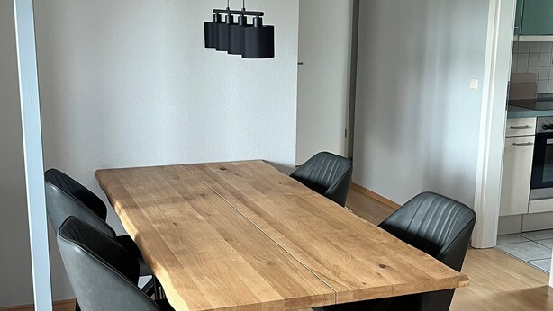 Zona pranzo con tavolo in legno, sedie nere e lampadario.