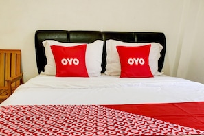 A bed with a black headboard, two pillows with 'OYO' text, and a patterned red and white bedspread.