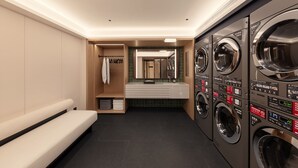 A modern laundry room with multiple washing machines, a bench, and a mirror.