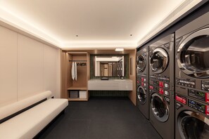 A modern laundry room with multiple washing machines, a bench, and a mirror.
