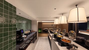Un espace dédié au petit-déjeuner à l’hôtel, avec un buffet, une machine à café et une vue sur le hall d’entrée.