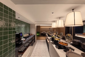 Un espace dédié au petit-déjeuner à l’hôtel, avec un buffet, une machine à café et une vue sur le hall d’entrée.