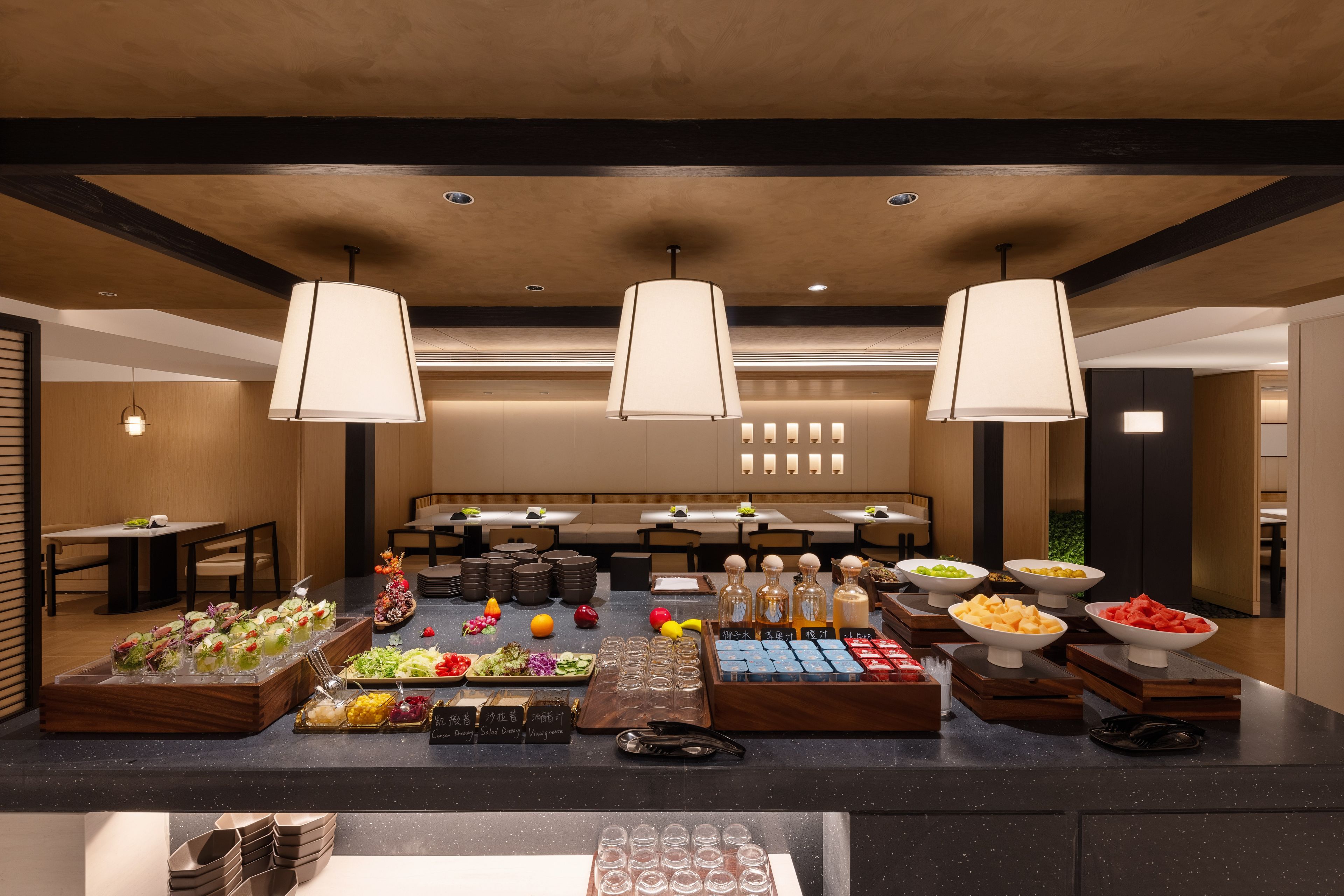 Un espai de buffet amb diverses platelles de menjar i distribuïdors de begudes, diverses zones d'estar i il·luminació penjant.