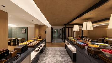 A modern hotel lobby with a central food display, seating areas, and a view into the corridor.