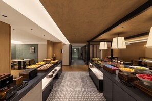 Un hall d’hôtel moderne avec un espace central où sont exposés des plats, des coins salon et une vue sur le couloir.