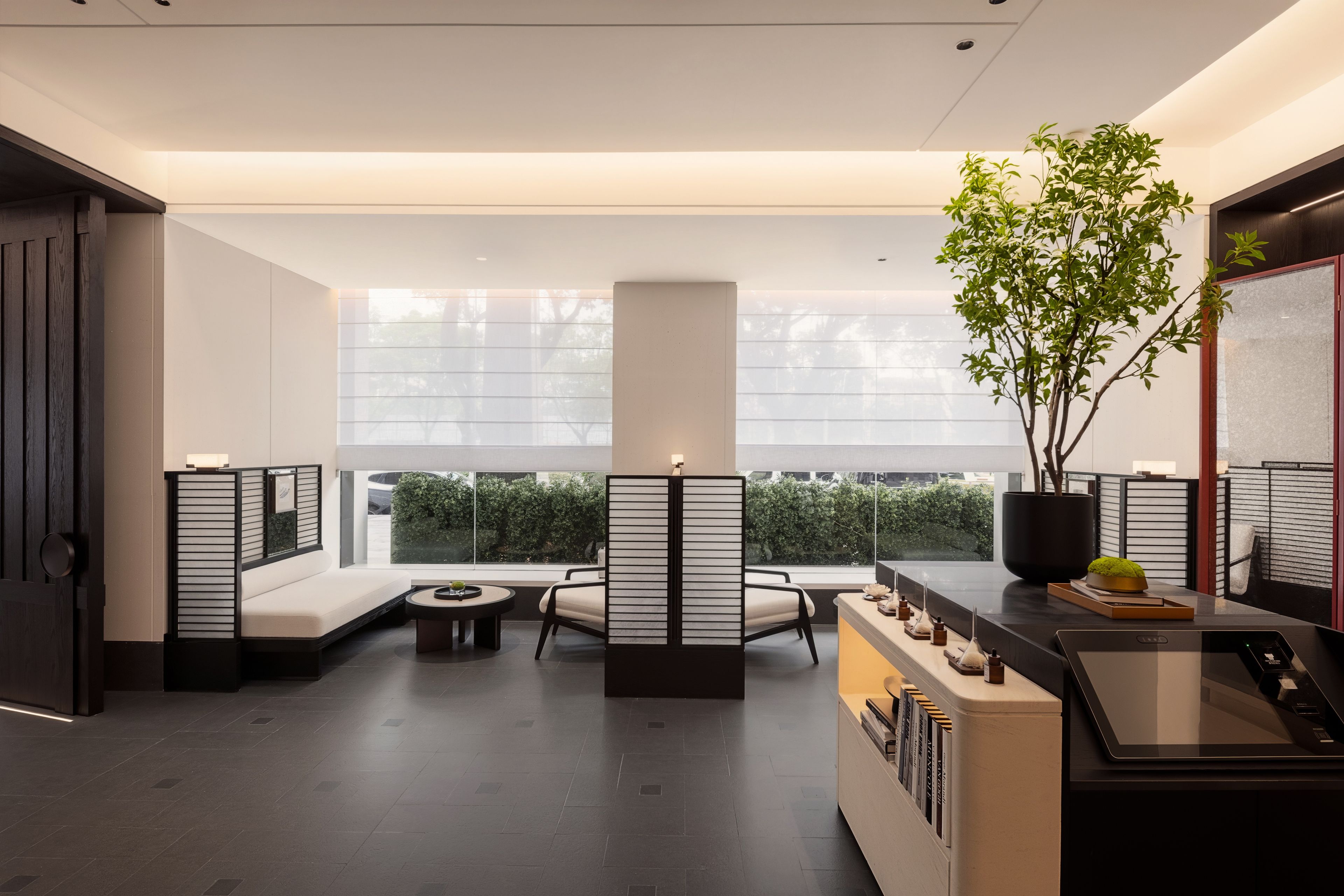 A modern interior with a seating area, a reception desk, and a view of greenery outside.