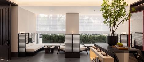 A modern interior with a seating area, a reception desk, and a view of greenery outside.