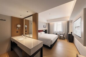 Une chambre d’hôtel avec un grand lit, un bureau, une chaise, un grand miroir et une salle de bain équipée d’un lavabo et de deux miroirs ronds.