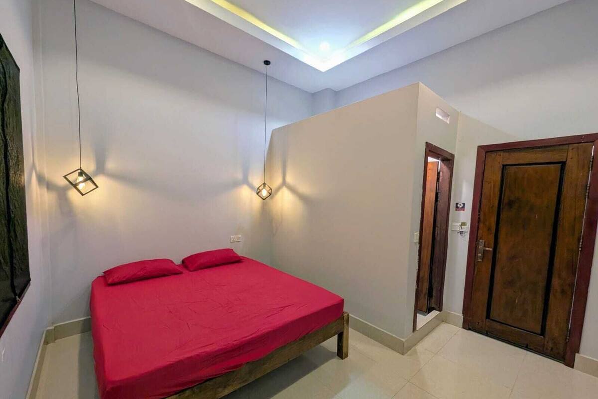 Un dormitorio con una cama, dos luces fijadas a la pared, una puerta y una lámpara en el techo.