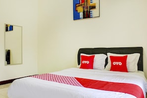 A hotel room with a bed, two red pillows with 'OYO' text, a large mirror, and a painting on the wall.