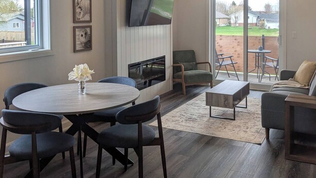 Una sala de estar moderna con chimenea, un comedor con una mesa redonda y sillas, y vistas al exterior a través de amplios ventanales.