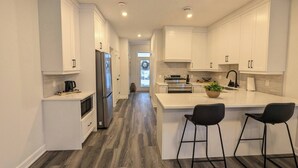 Una cocina moderna con armarios blancos, un refrigerador de acero inoxidable y una isla central con dos taburetes de bar.