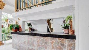 Un área de recepción con mostrador de piedra, plantas en macetas y una escalera que sube a un nivel superior.