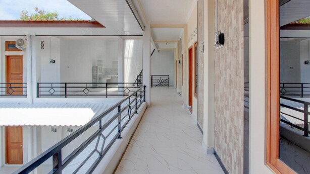 Un pasillo con balcón, puerta de madera y pared con azulejos.