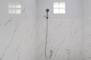 Une salle de bain aux murs recouverts de marbre, une douche équipée d’un pommeau de douche à main et une fenêtre ornée d’un motif géométrique.
