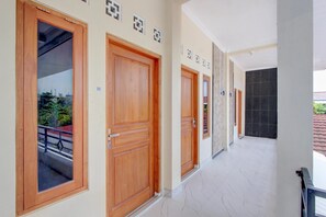 A corridor with wooden doors, a tiled floor, and a view of greenery outside. - Teratai Inn Deluxe Comfort (Yogyakarta)
