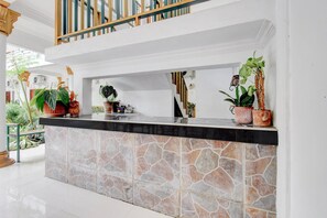 A reception area with a stone counter, potted plants, and a staircase. - Teratai Inn Deluxe Comfort (Yogyakarta)