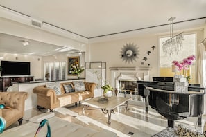 Ein Wohnzimmer mit einem schwarzen Klavier, beigefarbenen Sofas, einem Couchtisch und einem Kamin.