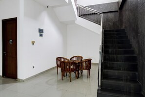 Uma escada com corrimão de metal, uma porta de madeira e uma mesa com cadeiras em um corredor.