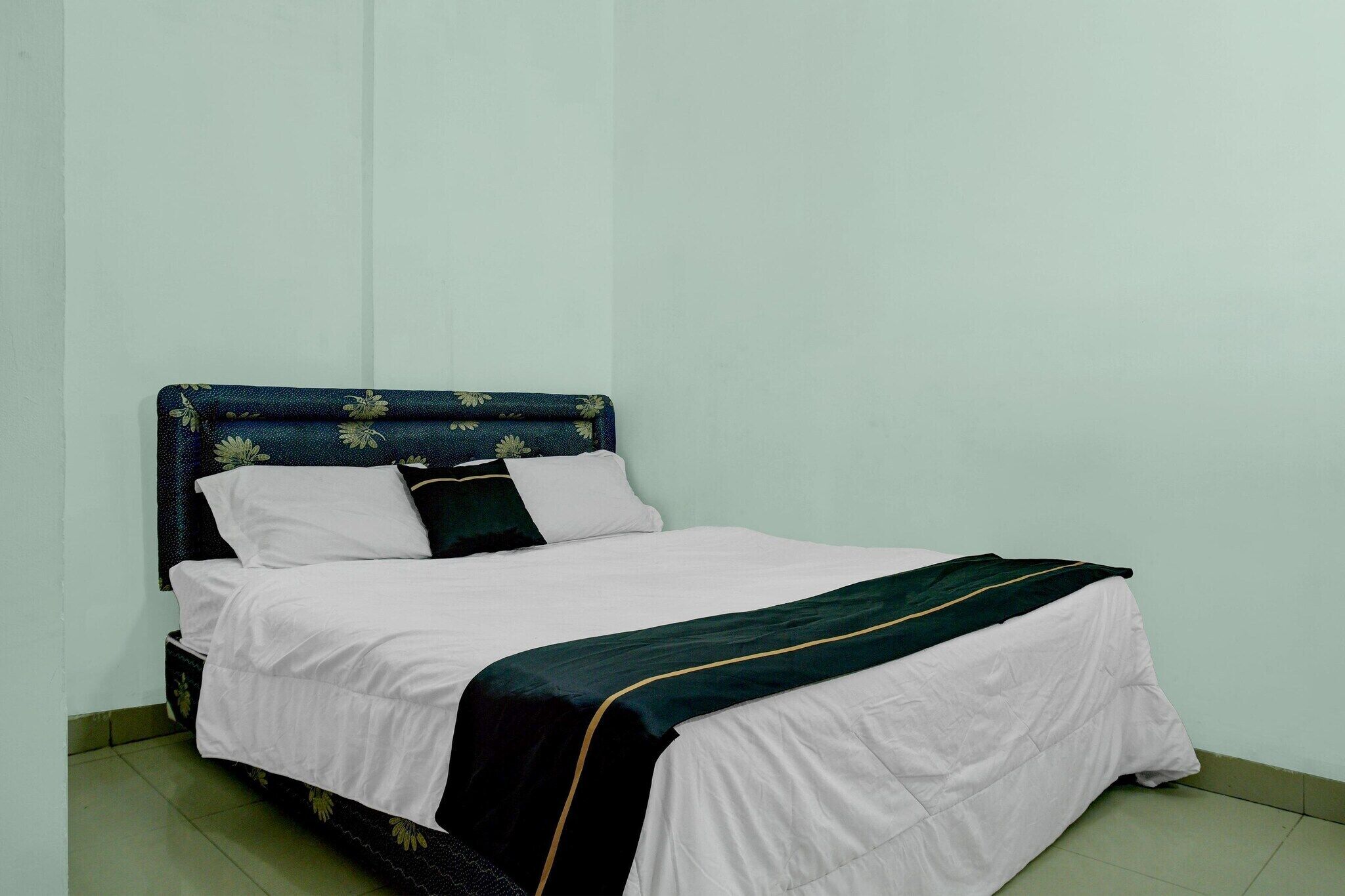A single bed with a dark headboard and white bedding in a room with plain walls and a tiled floor.