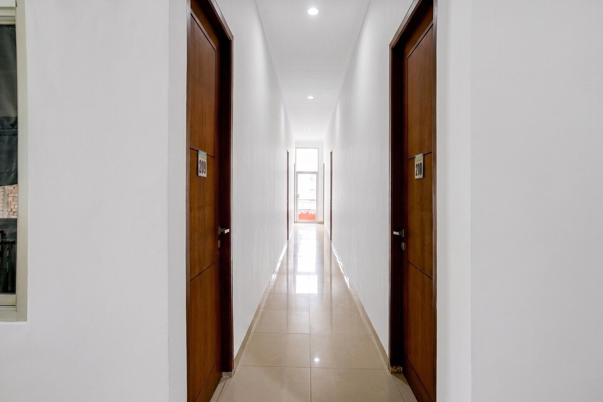 Un pasillo largo y estrecho con puertas de madera a ambos lados, que conduce a una habitación luminosa al final.