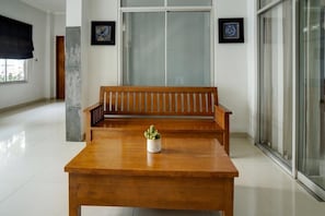 A wooden bench with a potted plant in the center, a tiled floor, and a large glass door in the background.
