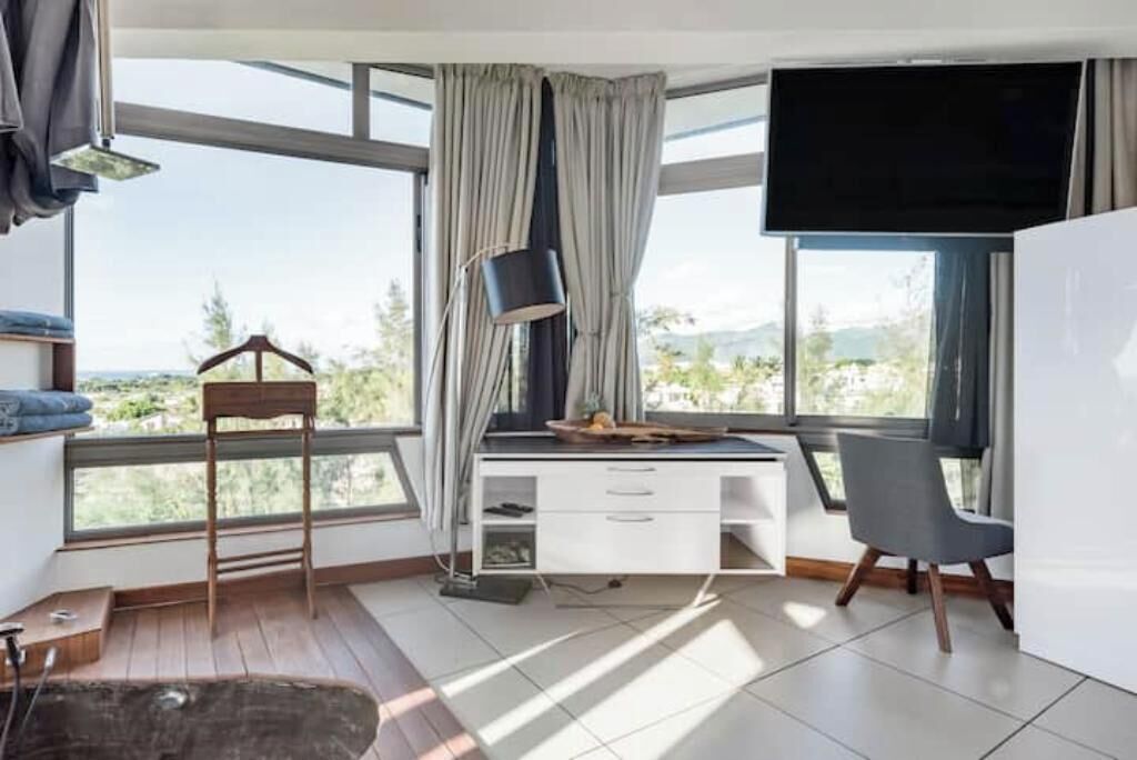 Een kamer met een bureau, stoel en grote ramen met uitzicht op de omgeving.