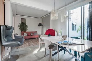 A modern living room with a dining table, a sofa, a chair, and a potted plant.