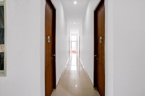 A long, narrow hallway with wooden doors on either side, leading to a bright room at the end.