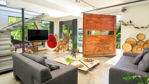 A modern living room with grey sofas, a flat-screen TV, a red chair, and a staircase leading to a balcony. - Private tropical loft in shared villa + pool + jacuzzi (Port Louis)