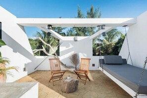A rooftop patio with two wooden chairs, a small round table, and a hanging swing.