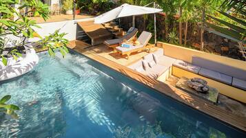 Un espace aménagé au bord de la piscine, avec des chaises longues, un parasol et un mur en pierre.