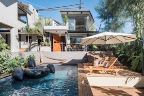 A modern pool area with a floating ring, lounge chairs, and an umbrella.