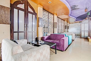 A spacious lobby with a high ceiling, a large seating area with sofas, a coffee table, and a decorative wall with geometric patterns.