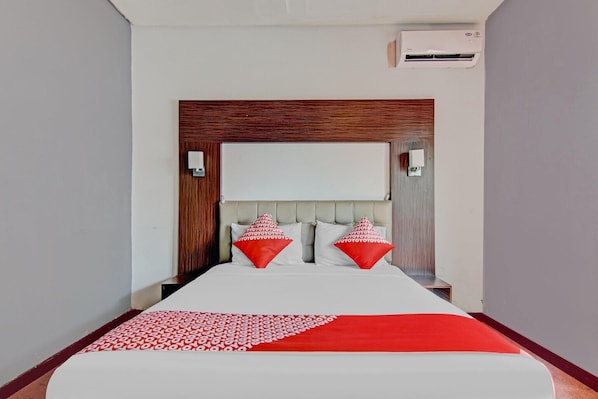 Une chambre d’hôtel comprenant un lit, une tête de lit, deux tables de chevet et un appareil de climatisation.