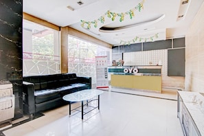 A modern hotel lobby with a black sofa, a glass coffee table, a reception desk, and a patterned wall.