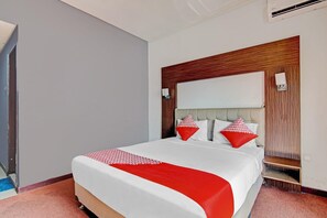 A hotel room with a bed, a wooden headboard, a red and white bedspread, and a red pillow.