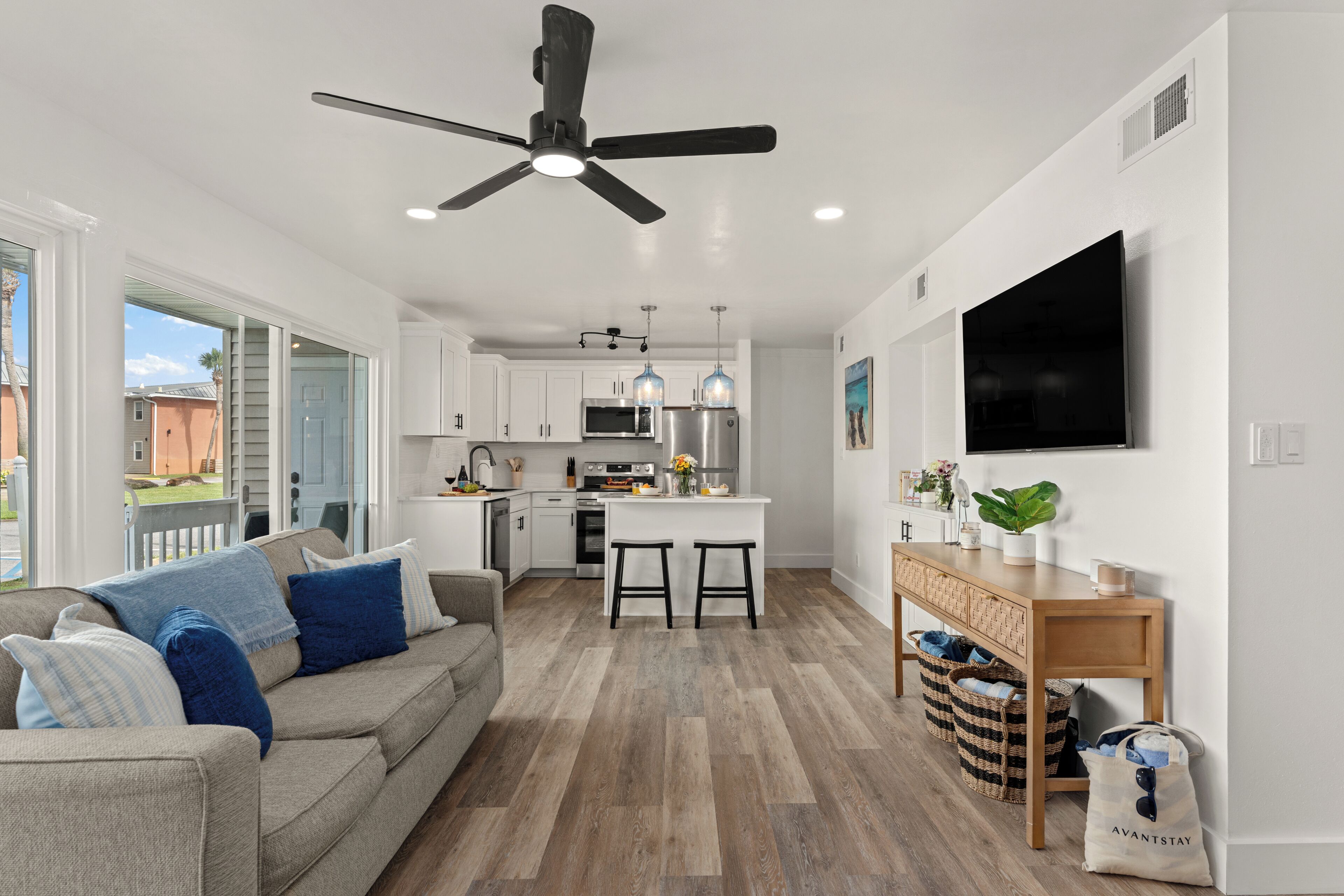 A modern kitchen with a central island, a dining area with a sofa, and a TV mounted on the wall.