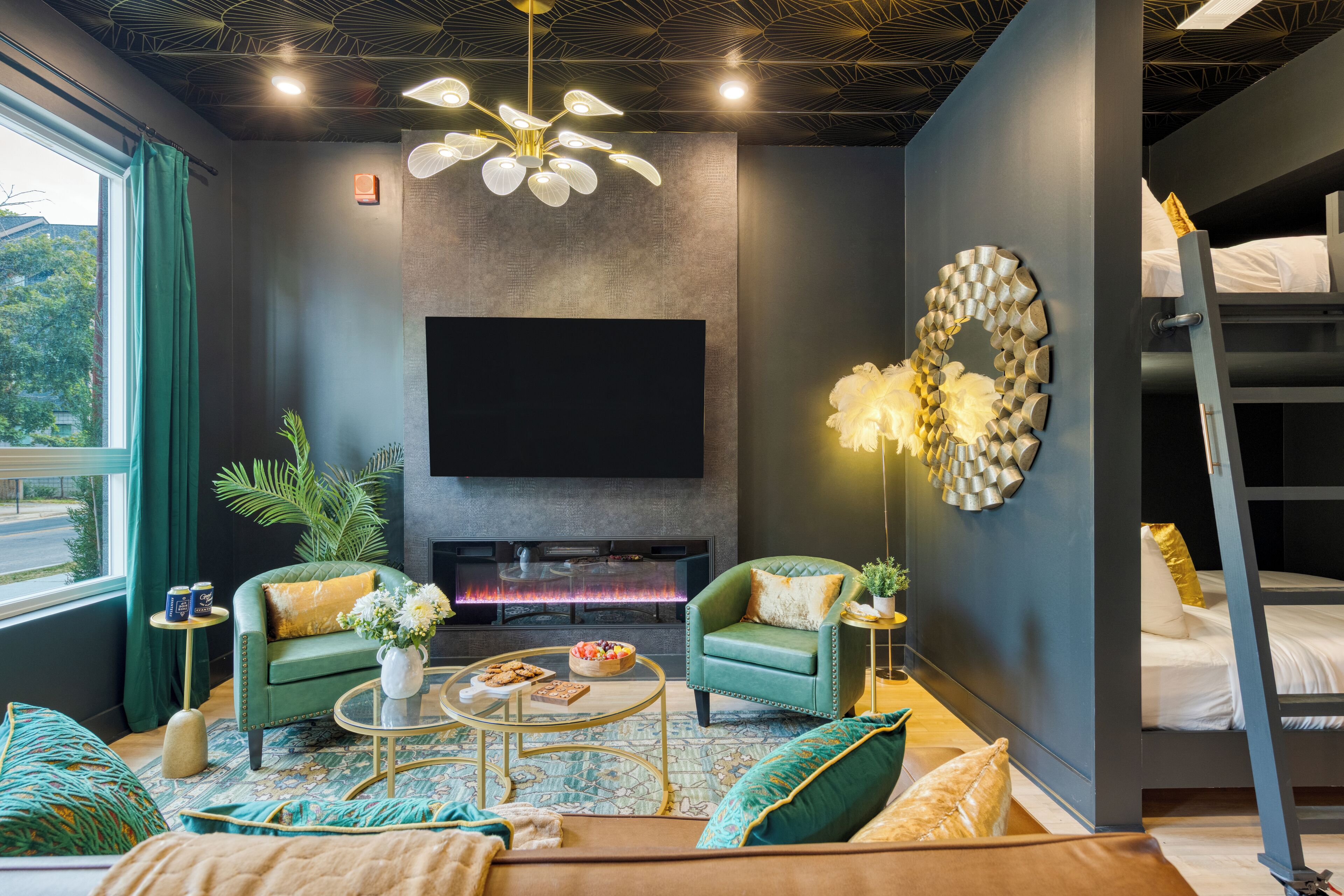 A modern living room with a fireplace, two green armchairs, a coffee table, and a large flat-screen TV mounted on the wall.
