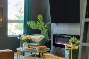 Ein Wohnzimmer mit einem grünen Sofa, einem Glastisch, einem Kamin und einer Topfpflanze.