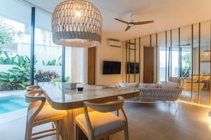 Ein modernes Interieur mit Essbereich, Bar und Deckenventilator, sowie ein großes Fenster mit Blick auf einen Pool.