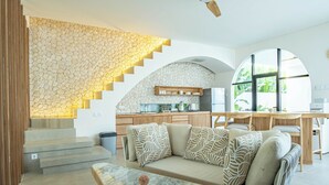 Un interior moderno con una pared de piedra, un sofá con cojines estampados, una mesa de centro de mármol y una zona de cocina con armarios de madera.