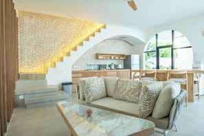 A modern interior with a stone wall, a sofa with patterned cushions, a marble coffee table, and a kitchen area with wooden cabinets. - Kona Resort Pererenan (Canggu)