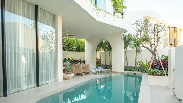 Una piscina interior moderna con agua cristalina, rodeada de plantas y mobiliario.